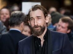 a man with a beard and black shirt is looking off to the side in front of a crowd