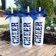 three white tumbles with blue bows are sitting on a wooden table in front of some flowers