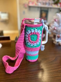 a crocheted coffee cup holder with a pink and green handle on a wooden table