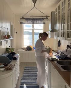 a woman standing in a kitchen next to a sink and counter top with dishes on it