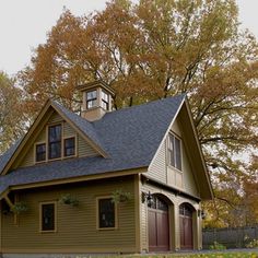 a green house with a brown roof and two dormers on the second floor is surrounded by autumn foliage