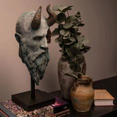 a vase with a plant and a statue of a demon next to it on a table