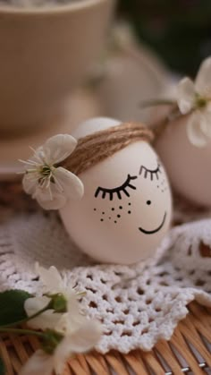 two eggs with faces painted on them are sitting on a doily next to a cup and saucer