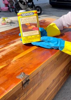 a wooden table topped with a yellow and blue glove next to a can of furniture refinishment