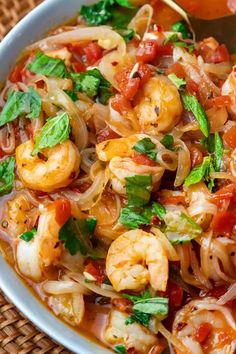 a white bowl filled with pasta and shrimp on top of a woven place mat next to a wooden table