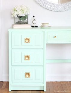 a mint green desk with gold handles and drawers in front of a round mirror on the wall