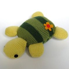 a knitted turtle toy with a flower on its head, sitting on a white surface