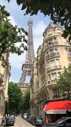 the eiffel tower is in the background of this street lined with parked cars