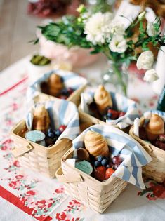 small baskets filled with fruit sitting on top of a red and white table cloth next to flowers