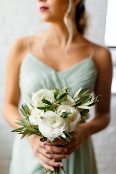 a woman in a green dress holding a bouquet of white roses and greenery on her wedding day