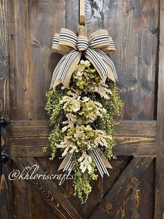 a wreath hanging on the side of a wooden door decorated with flowers and greenery