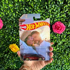 a person holding up a hot wheels die cast car in front of some pink roses