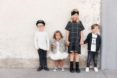 three children standing next to each other in front of a white wall wearing black and grey clothing