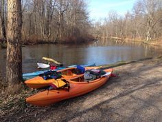 two kayaks sitting on the side of a river next to a tree and some canoes