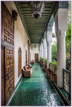 a long hallway with green tile floors and wooden doors leading to the second floor, along with potted plants on either side