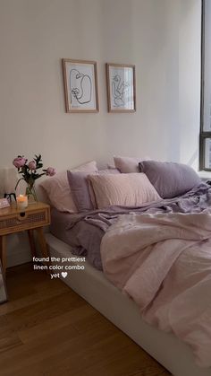 a bed with pink sheets and pillows next to a wooden table in front of a window