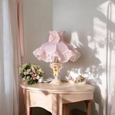 a table with a lamp on top of it next to flowers and a vase in the corner