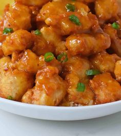 a white bowl filled with chicken covered in sauce and garnished with green onions