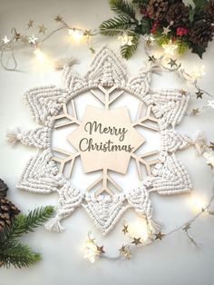 a wooden snowflake with the words merry christmas written on it surrounded by evergreen leaves and pine cones