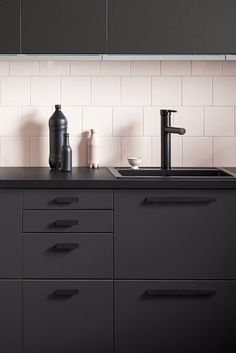 a kitchen with black cabinets and white tile backsplash, sink and faucet