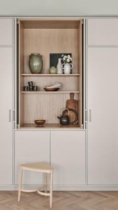 an open cabinet in the middle of a room with wooden flooring and white walls