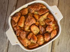 a white casserole dish filled with bread and cinnamon rolls on top of a wooden table