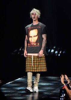 a man on the runway wearing a t - shirt and plaid skirt