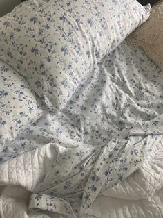 an unmade bed with blue and white flowers on the comforter, pillow and blanket