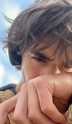 a close up of a person holding his hand to his face with the sky in the background