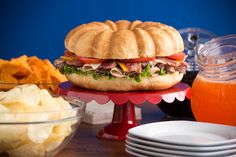 a large sandwich sitting on top of a red plate next to some chips and drinks