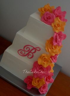 a three tiered cake decorated with flowers and the letter b on it's side