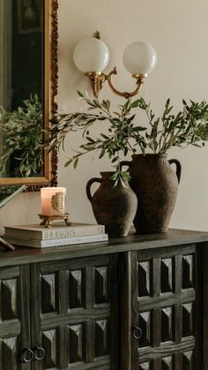 two vases with plants sit on top of a wooden cabinet next to a mirror