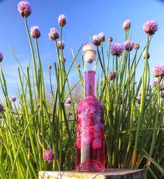 a bottle that is sitting on top of a stump in front of some grass and flowers