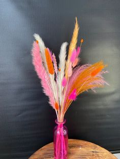 a pink vase filled with feathers on top of a wooden table