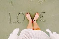 a woman's feet with the word love written in sand next to her legs