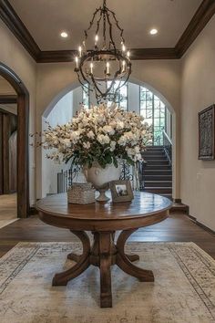 a table with flowers on it in the middle of a room that has stairs and chandelier