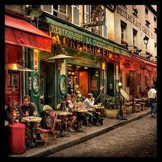 people sitting at tables in front of a restaurant on the side of a city street