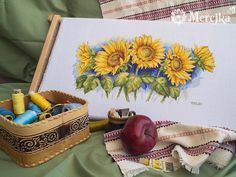 an apple and some thread on a table next to a canvas with sunflowers