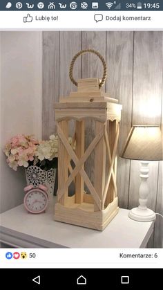 a wooden lantern sitting on top of a white table next to a lamp and flowers