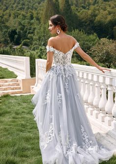 a woman in a long dress standing on the grass near a white fence and trees