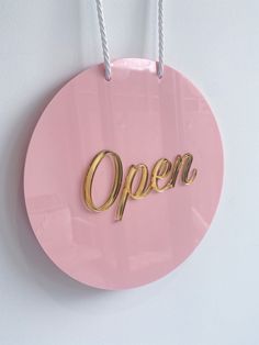 a pink sign with the word open hanging from it's side on a white wall