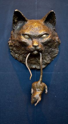 a bronze sculpture of a cat's head with a mouse attached to the wall