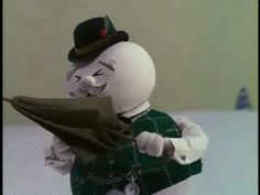 a white stuffed animal wearing a green dress and top hat holding a piece of paper