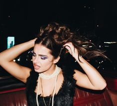 a woman sitting in a car with her hair up and wearing pearls on the neck