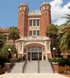 a large building with stairs leading up to the front door and palm trees in front