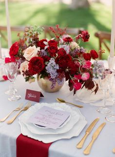 the table is set with red and white flowers, silverware, and place settings