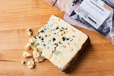 a piece of cheese sitting on top of a wooden table next to a bag of food