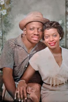 a man and woman sitting next to each other in front of a wall with flowers