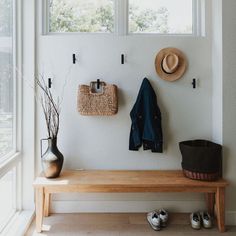 a wooden bench sitting under two windows next to a pair of shoes and a hat