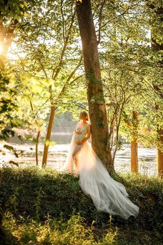 the bride and groom are posing for a photo in front of a tree at sunset